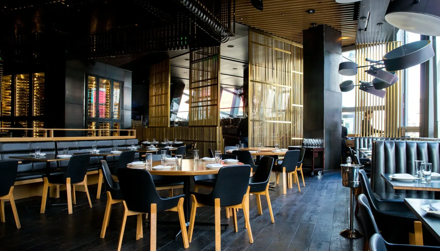 Futuristic restaurant interior with minimalist tables and warm ambient lighting through floor-to-ceiling glass windows at night