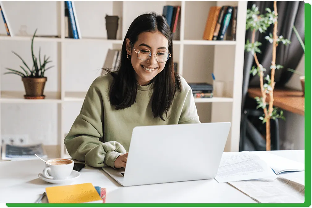 Woman smiling while working on a laptop at a desk with coffee