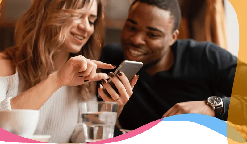 Two people smiling while browsing a food delivery app together on a smartphone