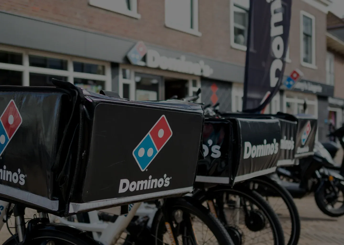 Domino's delivery bikes with branded delivery boxes parked outside a Domino's store