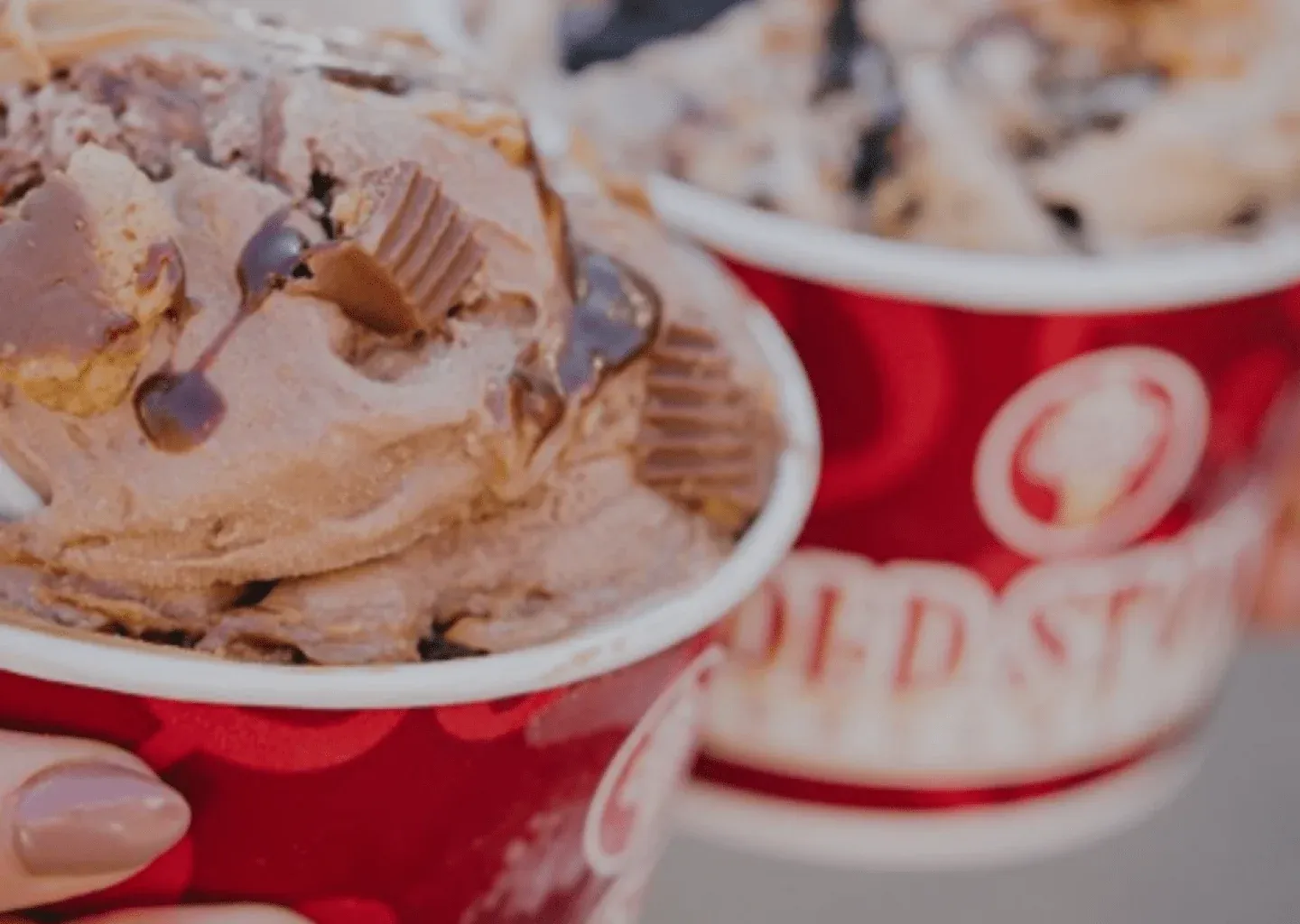 Two cups of Cold Stone ice cream topped with peanut butter cups and chocolate fudge