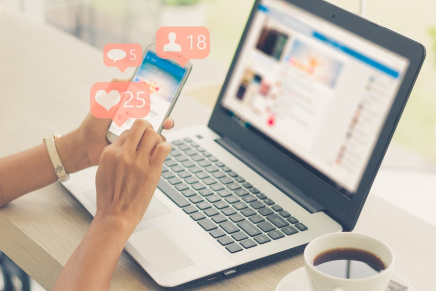 Person using a phone beside a laptop with social notification icons